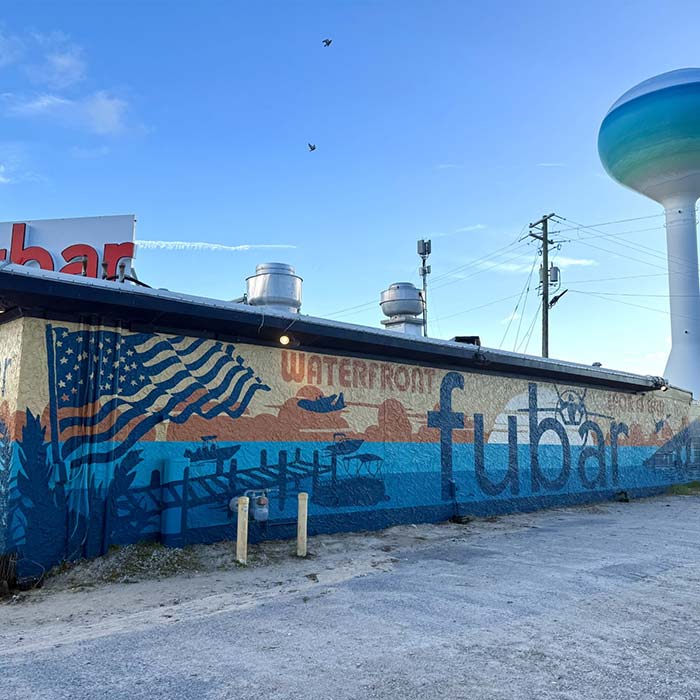 A mural says Waterfront Fubar with an American flag and FUBAR Pizza Bar water scene.